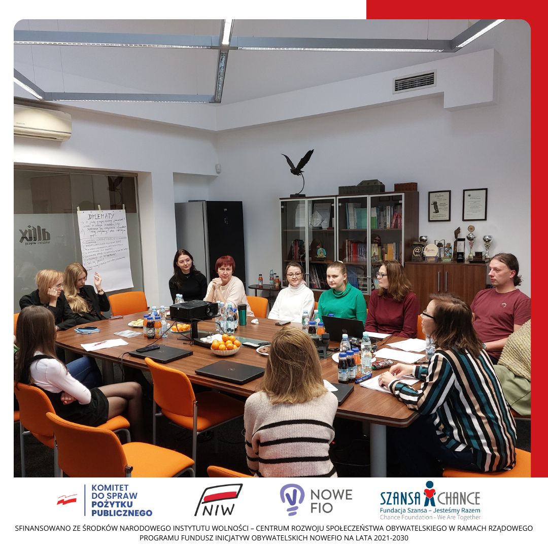 Grupa osób siedzi w sali konferencyjnej i słucha prezentacji kobiety.